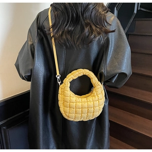Detailed view of a yellow quilted cloud bag worn as a shoulder bag on a dark jacket