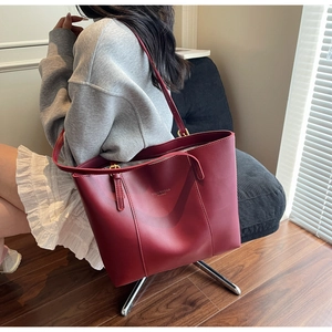Macro side view of wine red leather tote bag with long straps worn by a female model