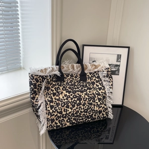 Fashionable leopard print tote bag with white fringes and black handles on a table