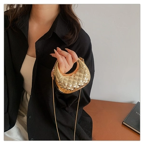Macro detail of gold quilted acrylic crescent bag with shiny metallic finish and chain