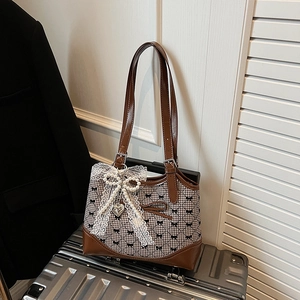 Sac sous le bras à carreaux avec nœud en dentelle et pendentif perle sur une valise