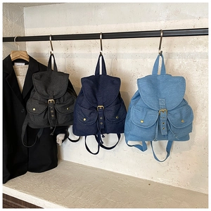 Three colors of denim backpacks with metal buckles displayed on a rack for travel
