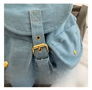 Close-up of golden metal buckle and rivet details on light blue denim backpack