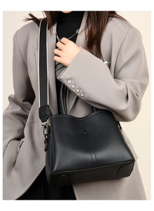 Detail of black lychee grain leather handbag with stylish wide canvas shoulder strap