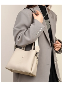 Detailed view of beige lychee grain leather handbag with wide shoulder strap on model