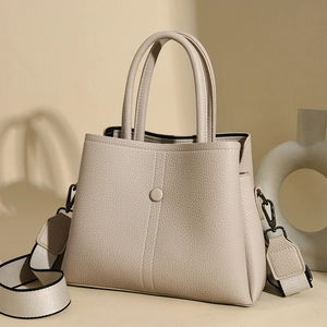 Close-up of litchi grain leather texture and wide fabric shoulder strap on beige handbag