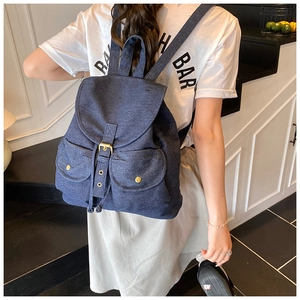 Detail of dark blue denim backpack with flap cover and metallic buckle on model