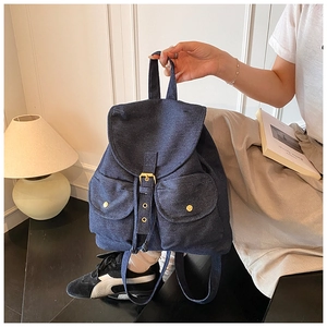 Detail of blue denim backpack showing magnetic flap pockets and metallic buttons