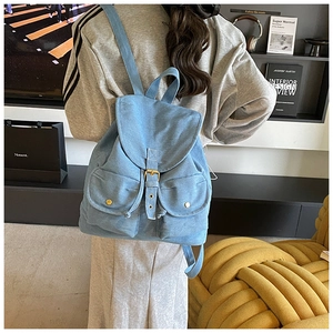 Detail of light blue denim backpack showing metal buckles and vintage pockets on model