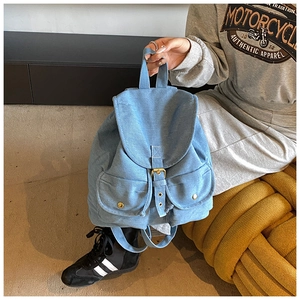 Detail of light blue denim backpack featuring flap closure and gold metal snap buttons