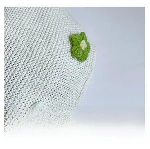 Macro shot of white knit fabric with green and white crochet flower details on tote bag