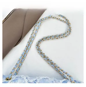 Détail d'une bandoulière en denim bleu clair avec chaîne en métal doré et bords effilochés