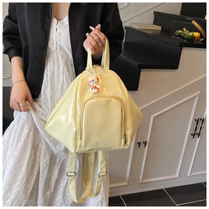 Close-up of a pale yellow glossy backpack with a cute white doll charm and silver zippers