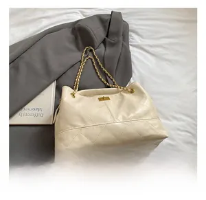 Detail of quilted leather tote bag with gold chain strap and metal clasp on grey blazer