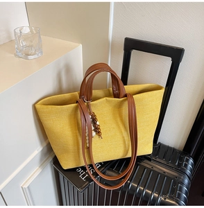 Detail of yellow canvas tote bag with brown leather handles placed on luggage