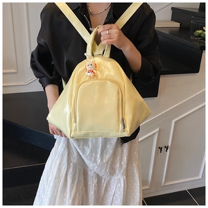 Close-up of yellow patent leather backpack with minimalist triangle design and astronaut charm