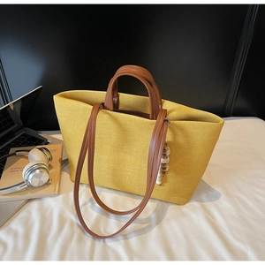 Detail of yellow canvas tote bag with brown leather handles and decorative beads on top