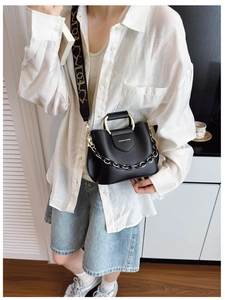 Detail of black tote bag with gold handle, thick metal chain, and vintage wide strap