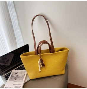 Detail of a large yellow canvas tote bag with brown leather handles and bead ornament