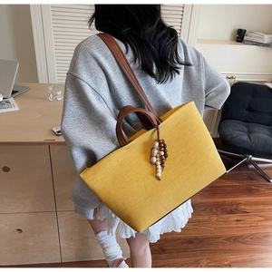 Detail of yellow canvas tote bag with wooden bead charm and brown straps on a shoulder