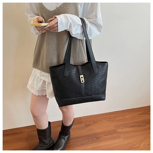 Macro detail of black woven leather tote bag featuring a gold rectangular twist lock
