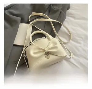 Detailed view of cream bow handbag with heart pendant and drawstring on grey fabric