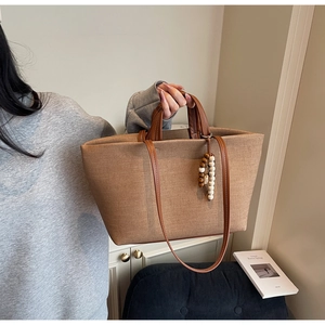 Close-up of brown canvas tote bag with leather handles and decorative wood bead charm