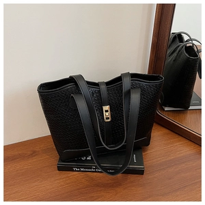 Detail of black woven tote bag with a golden turn-lock closure on wooden surface