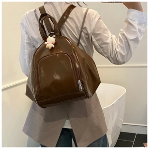 Detail of dark brown glossy PU leather backpack featuring adjustable straps and plush charm