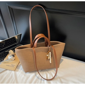 Detail of canvas tote bag showing brown leather handles and decorative wooden bead pendant