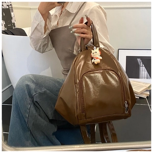 Close-up of brown glossy patent leather backpack with white rabbit pendant and front pocket