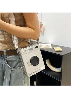 Detail of white camera-shaped crossbody bag with wide strap and embossed texture