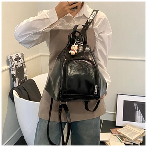 Detail of glossy black patent leather backpack featuring front zipper pocket and plush cat charm
