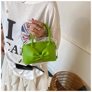 Detail of neon green bow-shaped handbag with golden heart charm and drawstring liner