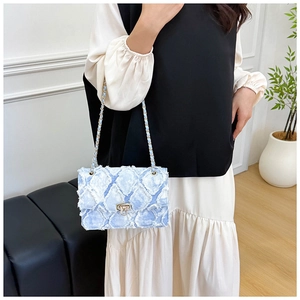 Détail du sac bandoulière en denim bleu clair avec matelassage effiloché et fermoir argenté