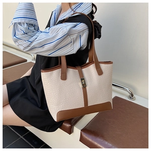 Detail of cream woven tote bag featuring brown leather trim and golden metal clasp