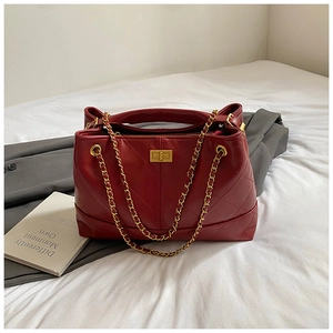 Close-up of wine red quilted handbag with golden chain strap and metallic clasp closure
