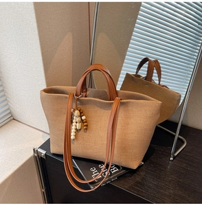 Close-up of textured canvas tote bag with brown leather handles and wooden bead charm