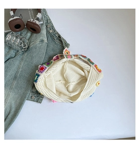 Close-up of white crochet tote bag with colorful floral knit patterns on a white table