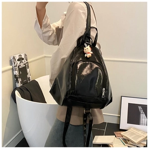Glossy black triangular backpack with silver zipper and a cute white cat plush charm