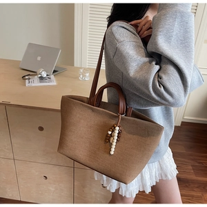 Detail of canvas tote bag with brown leather straps and natural wood bead tassel accessory