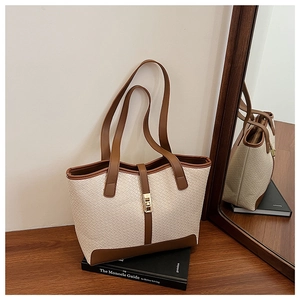 Detail of woven texture tote bag with brown straps and gold twist lock closure