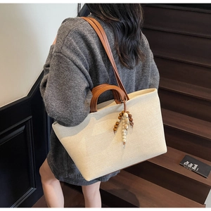 Detail of canvas tote bag with brown leather straps and decorative wooden bead tassel