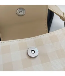 Detail of silver magnetic closure on beige checkered hobo bag with textured metal finish