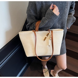 Detail of a beige canvas tote bag with brown straps and wooden bead fringe tassel decoration