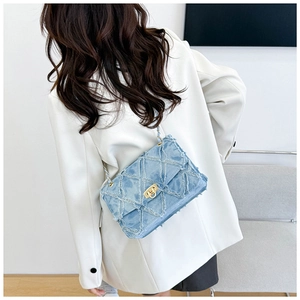 Détail d'un sac bandoulière en denim matelassé bleu avec chaîne dorée et bords effilochés