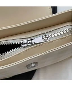 Detailed macro view of the silver metal zipper and magnetic snap on the beige textured bag