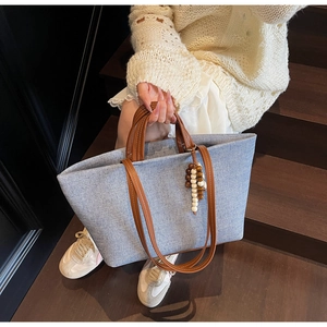 Light blue canvas tote with brown leather handles and wooden bead charm detail