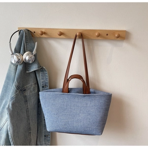Detail of blue denim tote bag with brown leather handles hanging on a wooden hook