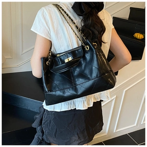 Detail of black quilted chain bag with gold metal lock clasp and leather strap